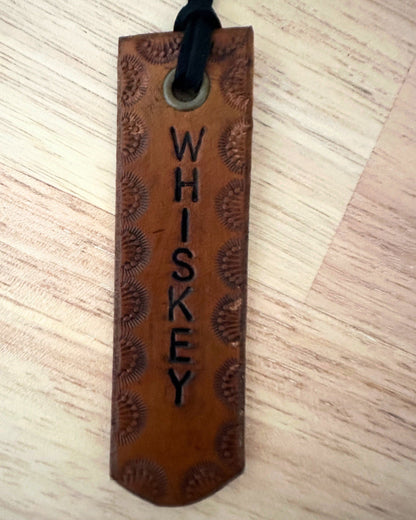 Brown leather tag with 'WHISKEY' engraving on a wooden surface