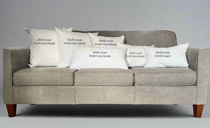 Gray sofa with decorative pillows labeled for size on a carpeted floor.