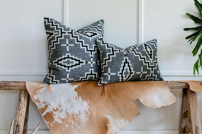 Two patterned pillows on a wooden bench with a cowhide rug underneath.