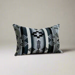 Decorative pillow with geometric pattern on a wooden bench against a white wall.