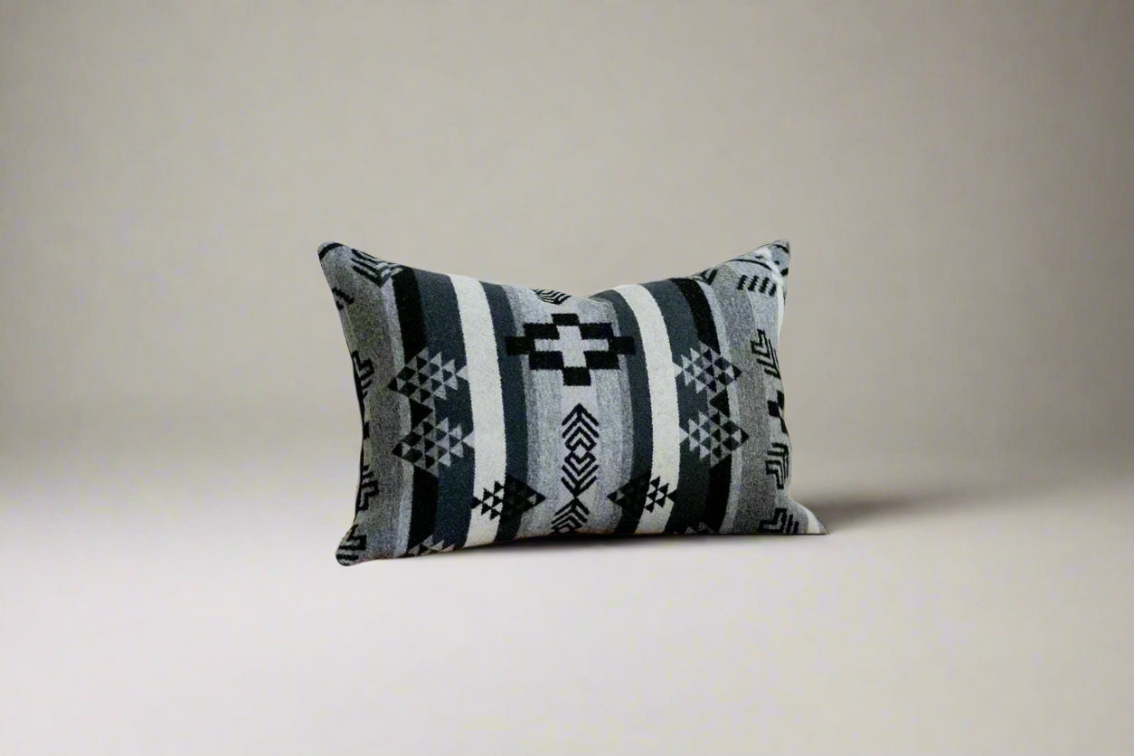 Decorative pillow with geometric pattern on a wooden bench against a white wall.