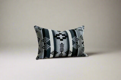 Decorative pillow with geometric pattern on a wooden bench against a white wall.