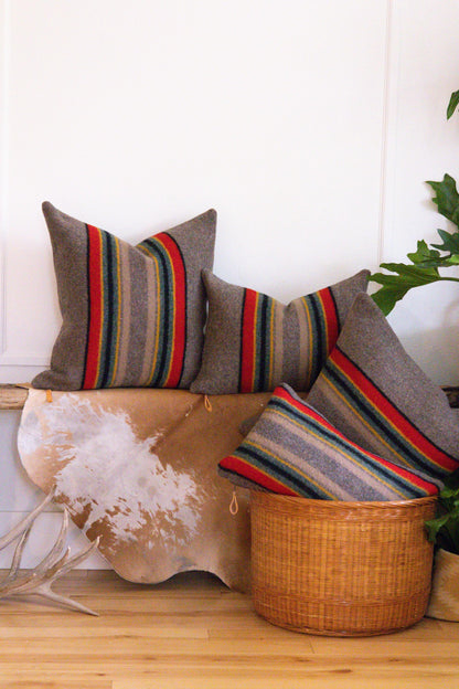 Decorative pillows with striped patterns on a wooden surface with a plant in the background