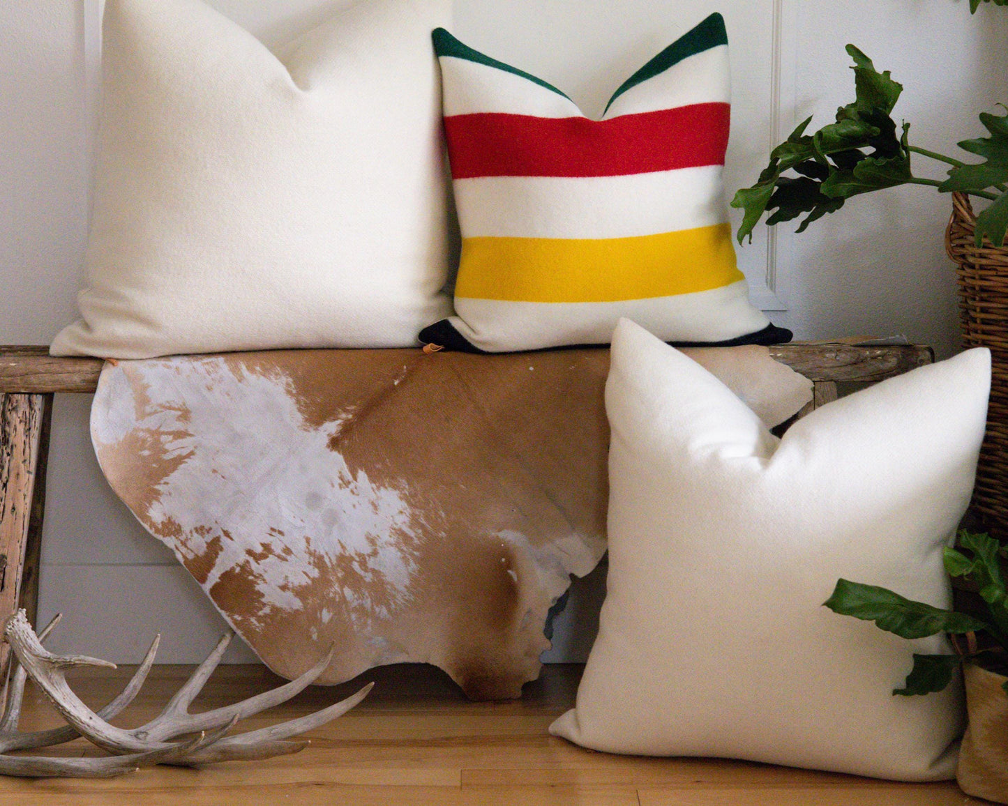 Decorative pillows on a wooden bench with a plant and antlers in the background