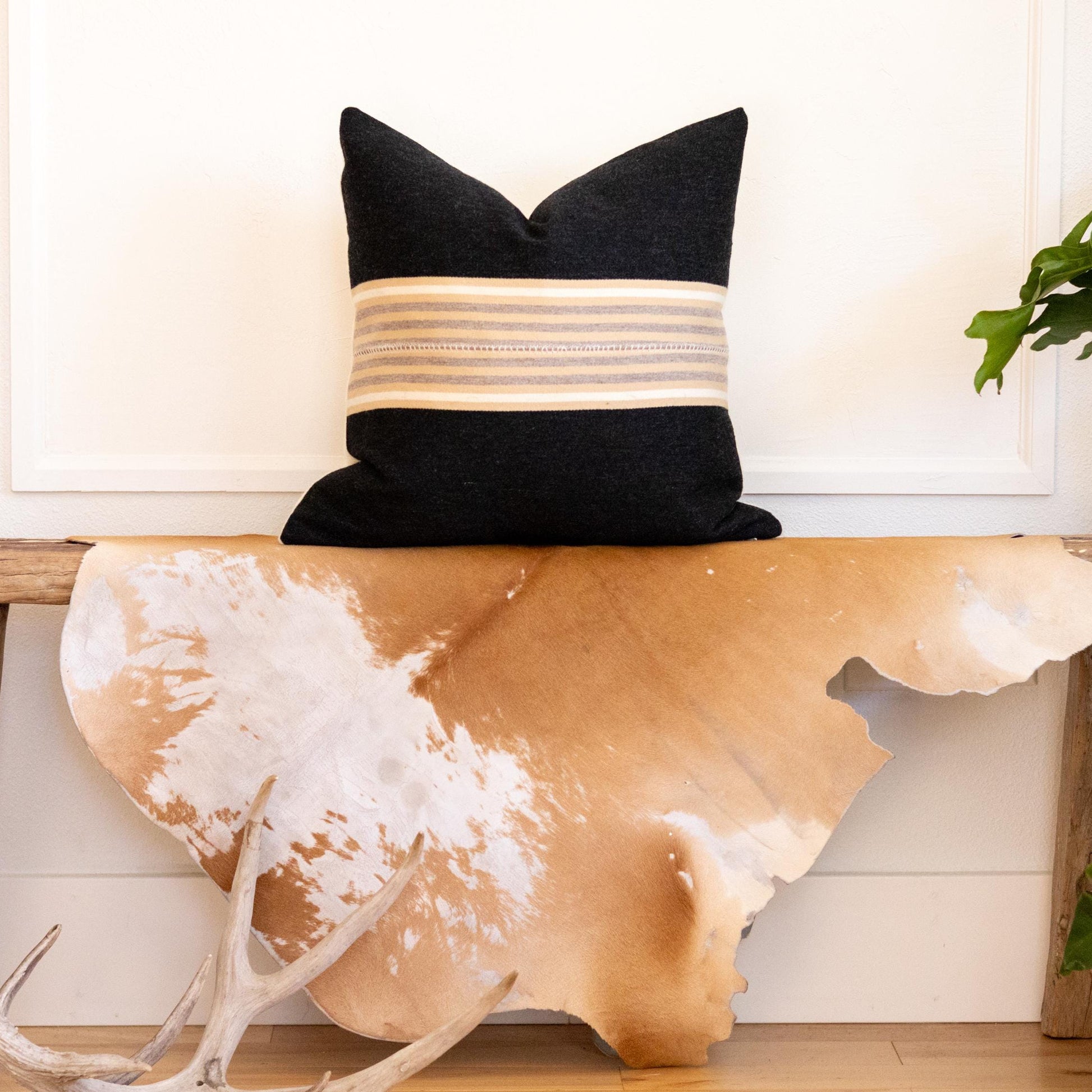Decorative pillow on a wooden bench with cowhide rug and plants