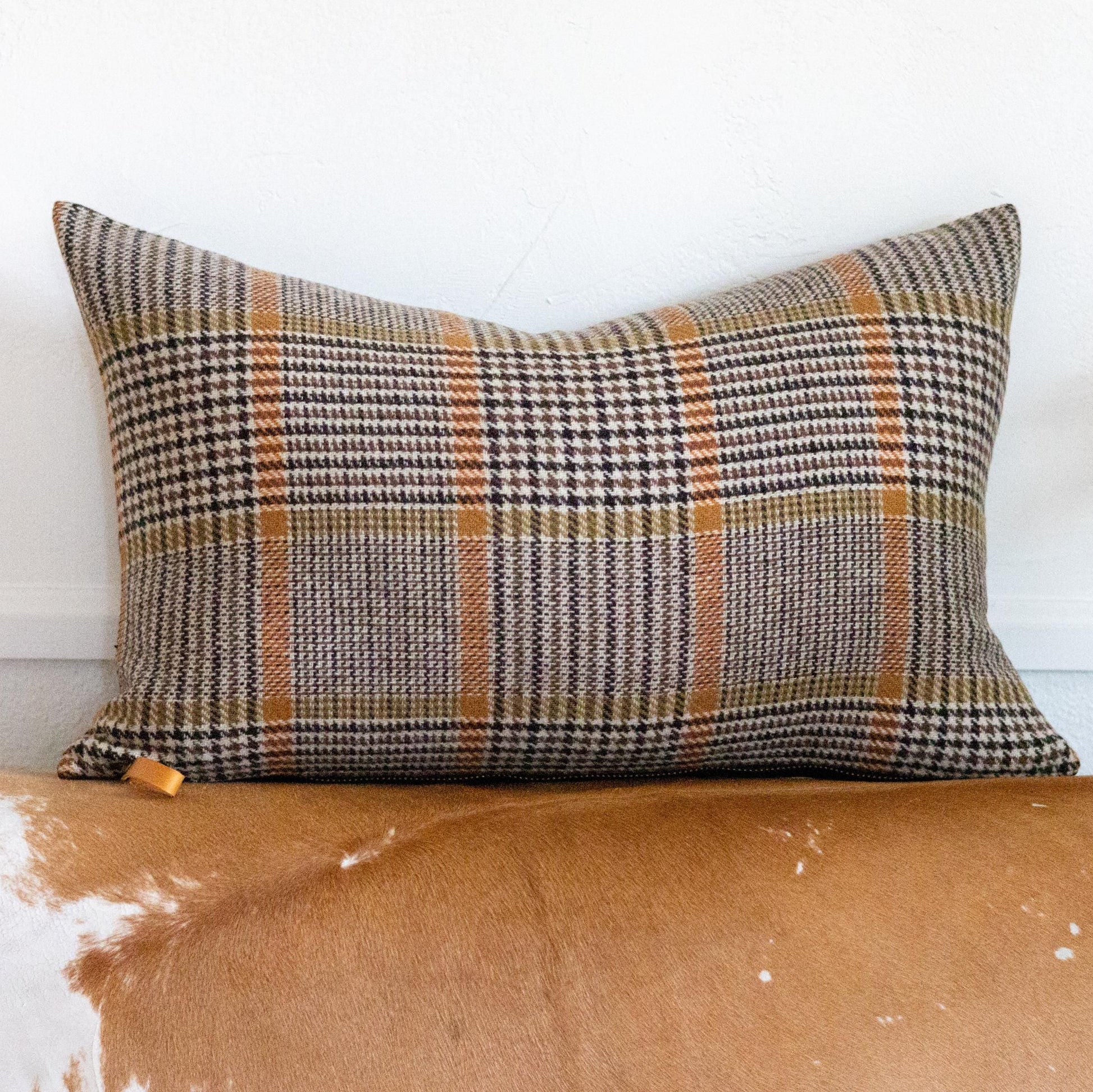 Plaid pillow on a worn leather couch with a white wall background