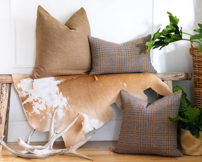 Decorative pillows on a wooden bench with a cowhide rug and antlers, against a white wall.