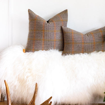 Plaid pillows on a white fur surface with wooden antlers in the foreground.