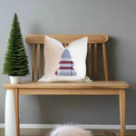 White pillow with a geometric pattern on a fluffy white chair next to a Christmas tree.