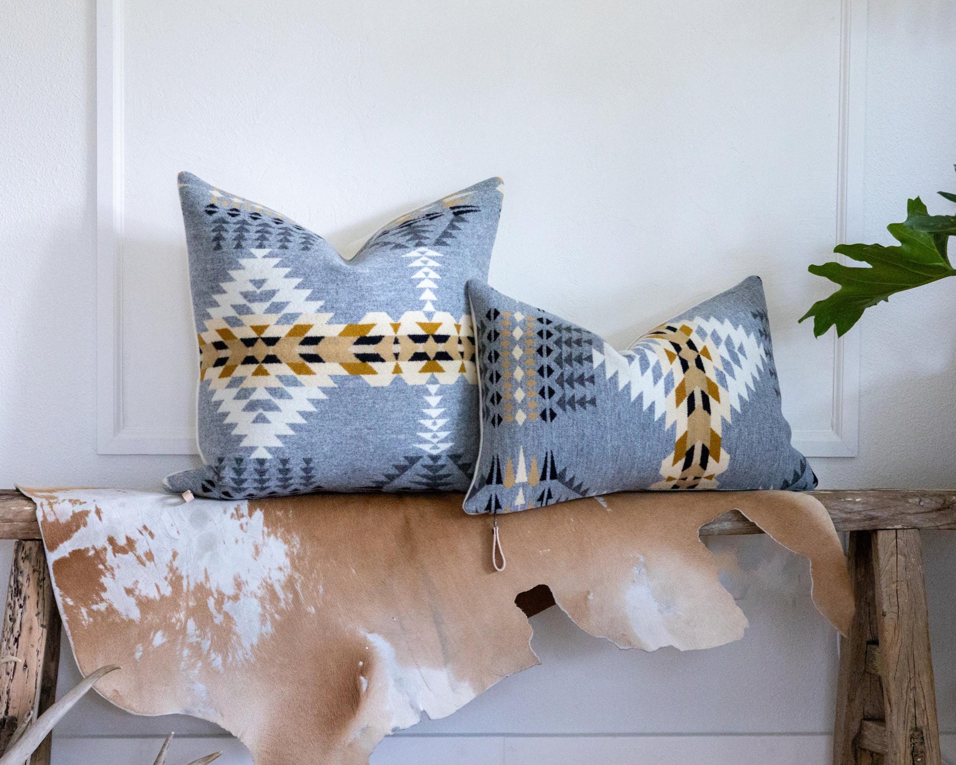 Two patterned pillows on a wooden bench with a cowhide rug against a white wall.
