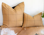 Two brown checkered pillows on a textured surface with a plant in the background