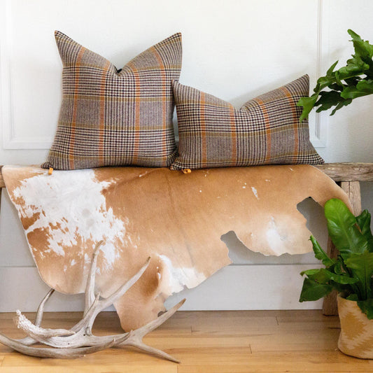 Plaid pillows on a bench with a cowhide rug and antlers in a room setting.