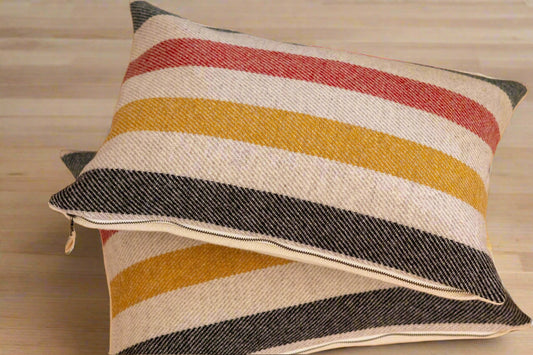 Striped pillow with red, yellow, and black colors on a wooden floor.