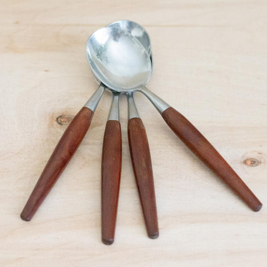 Set of four metal spoons with wooden handles on a light wood surface
