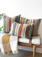 Colorful striped pillows on a wooden bench with a white wall background