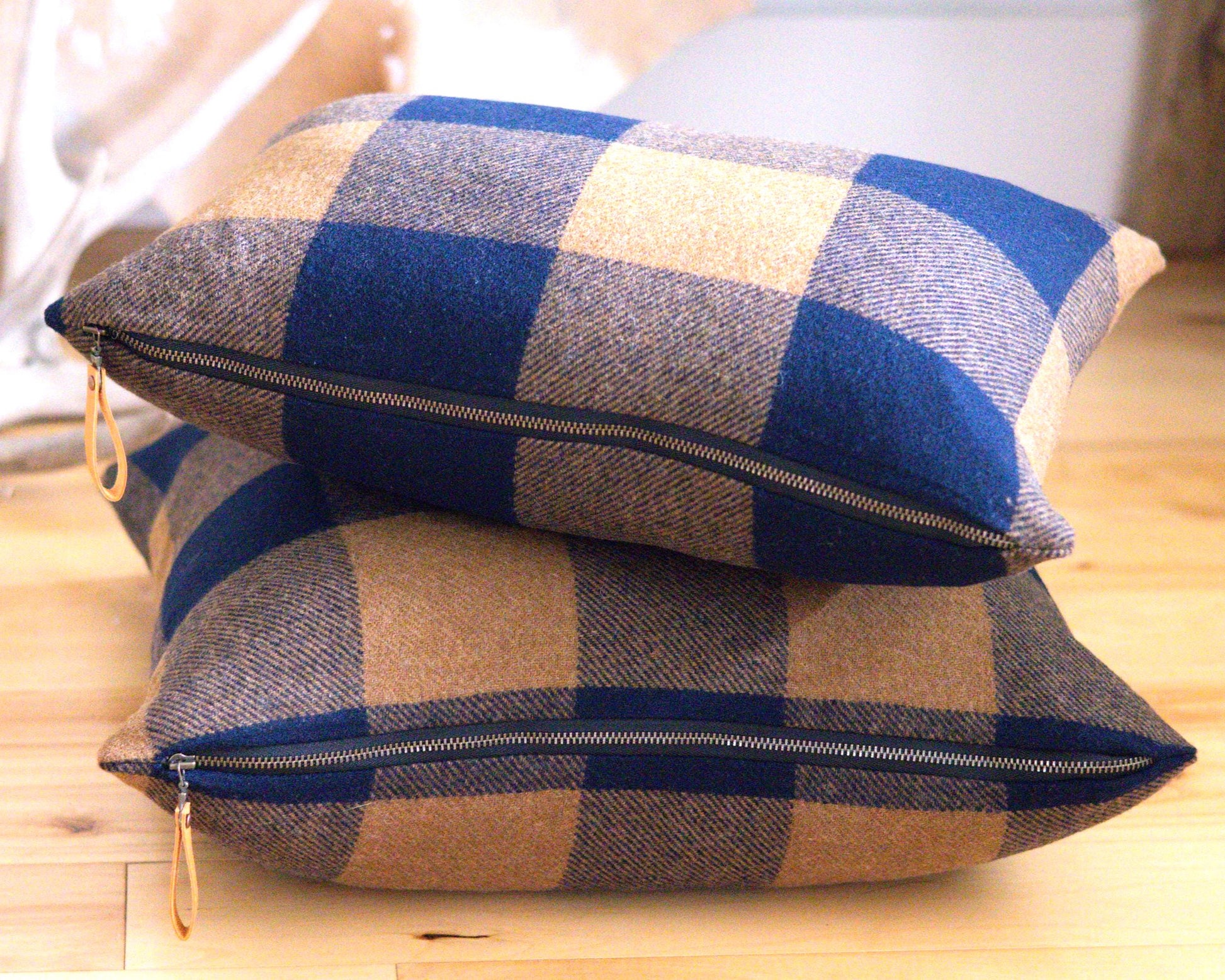 Two buffalo check patterned pillows with zippers on a wooden surface.